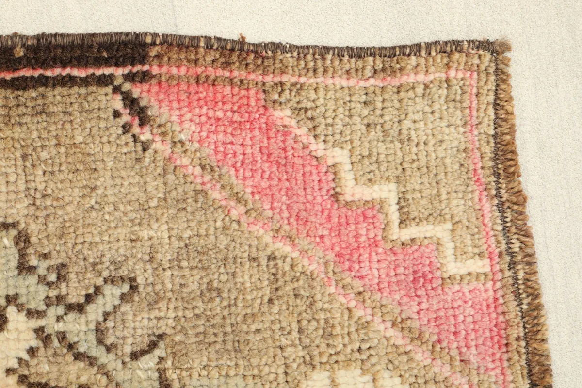 Close-up of the border design showing pink geometric shapes on the brown field