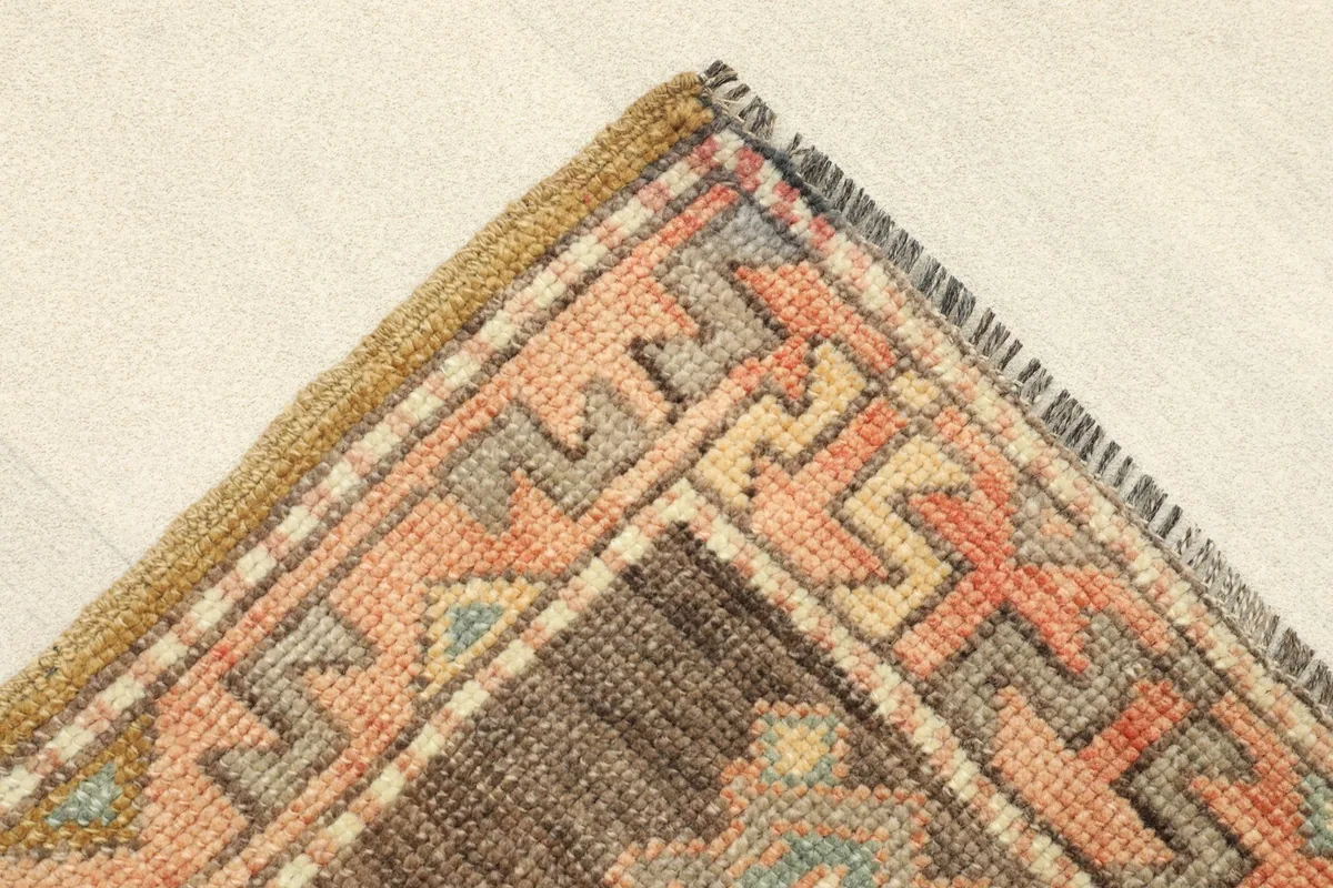 Corner detail of the rug, showing the geometric border pattern in rose, brown, and tan