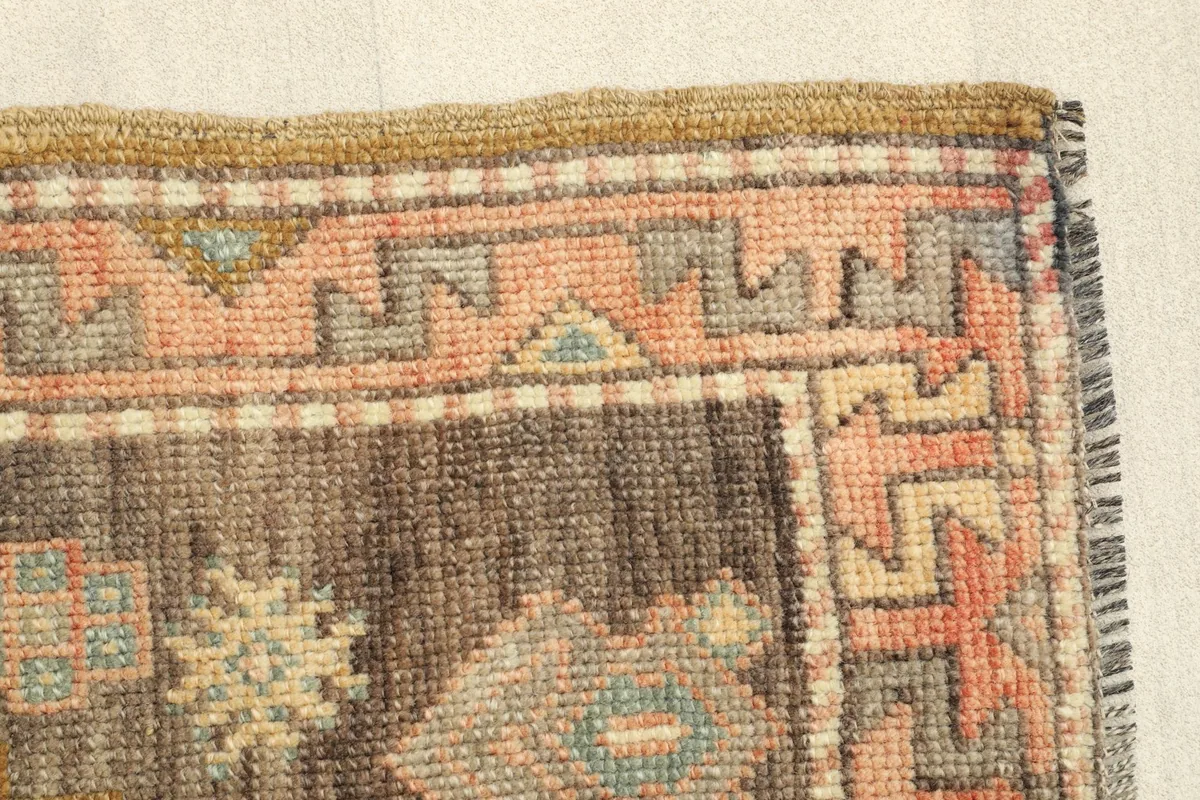 Edge detail of the hand-knotted rug, focusing on the muted rose and brown border design