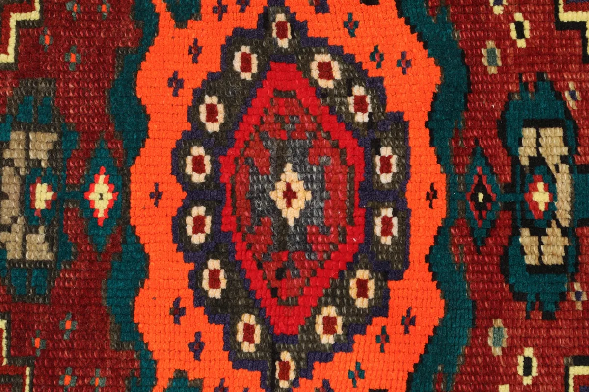 Close-up detail of the hand-knotted wool pile, showing the red, orange, green, and brown colors.