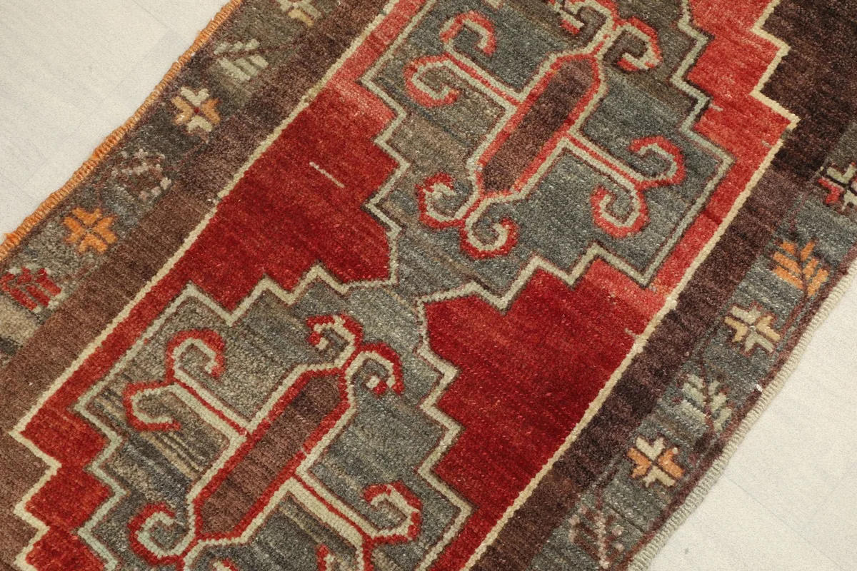 Angled view highlighting the central rust field and gray motifs of the wool rug