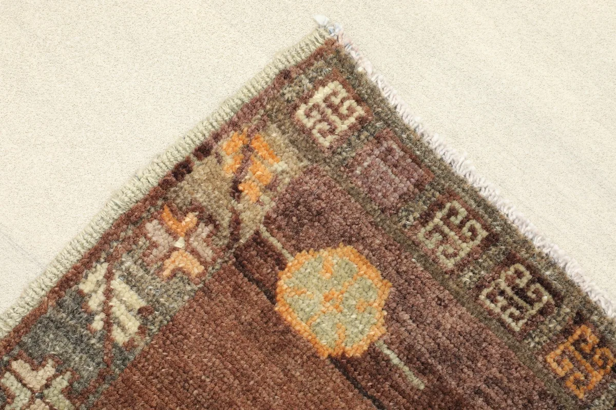 Corner detail showing the brown border with orange and olive accents and fringe