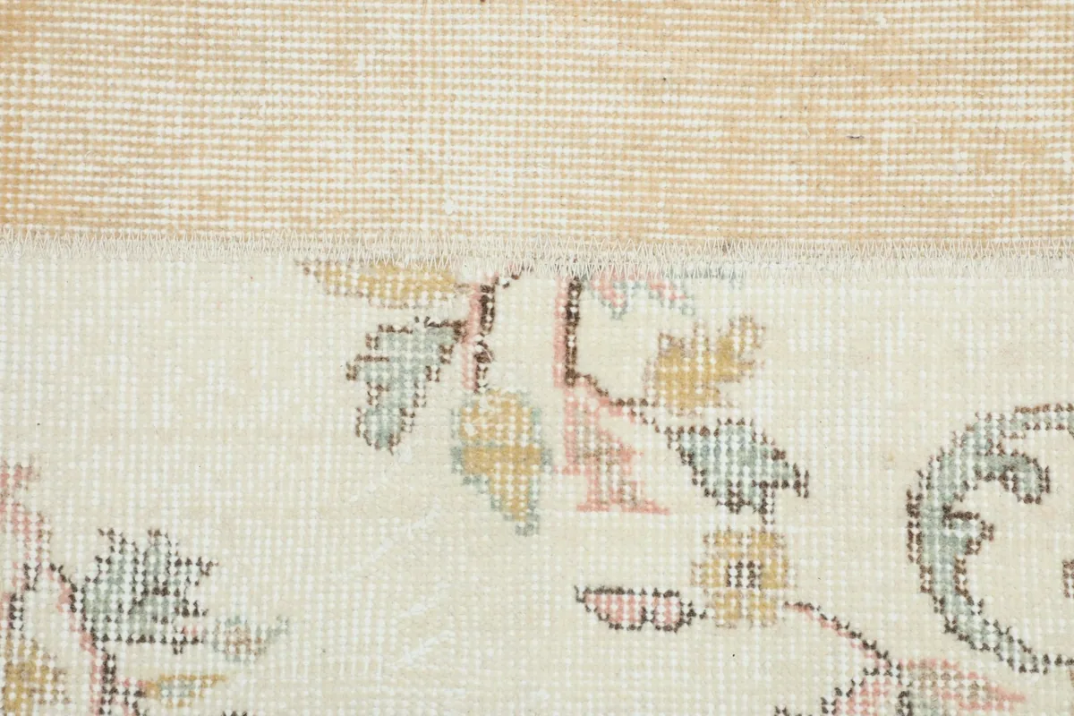 Close-up showing the low wool pile and a section of the cotton foundation with subtle floral design