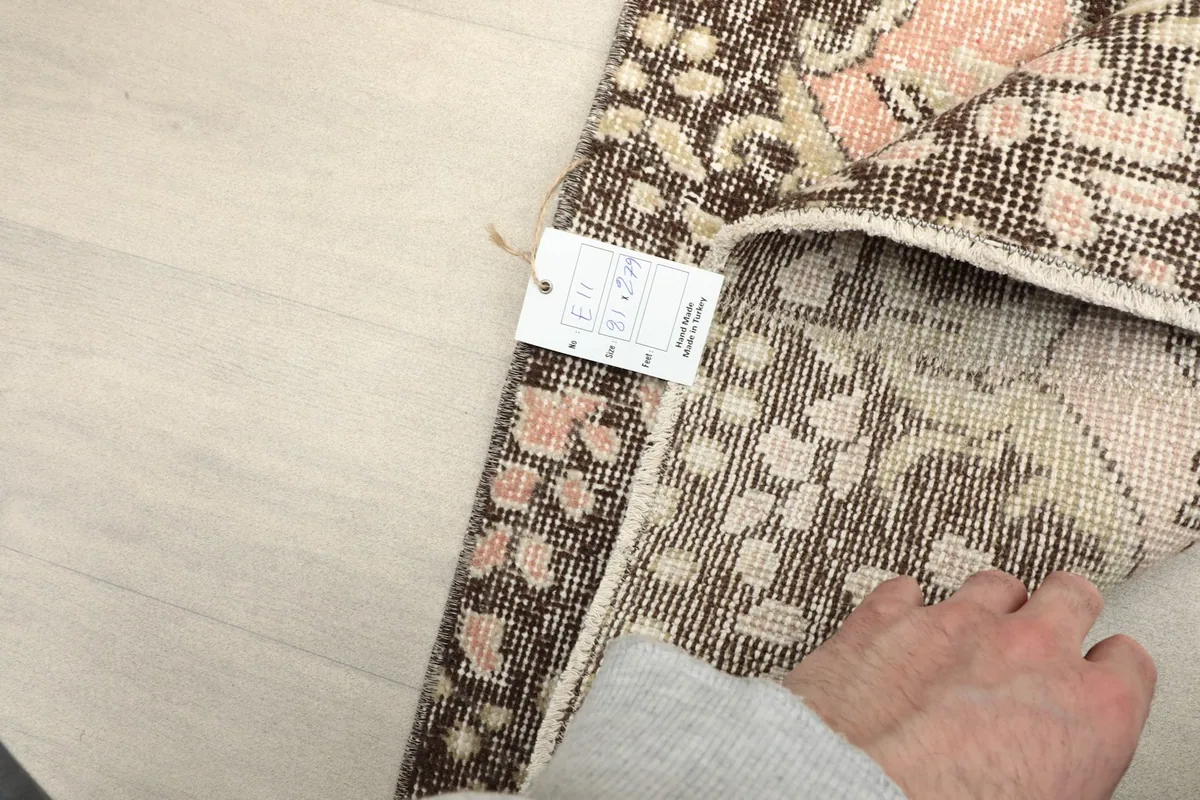 A hand holding the rug tag, showing the quality and origin details of the vintage Anatolian runner