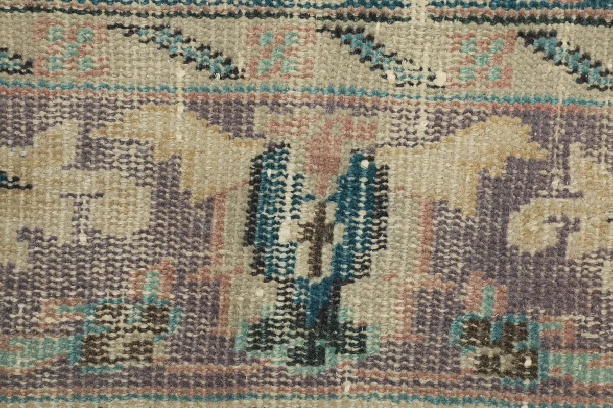 Macro detail of a purple and blue floral or tribal motif on a patch, showing the hand-knotted texture.
