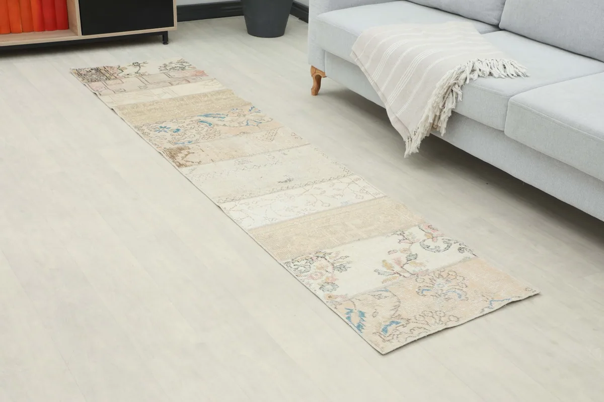 Angled view of the beige patchwork runner rug on a light floor, showing its length and design.