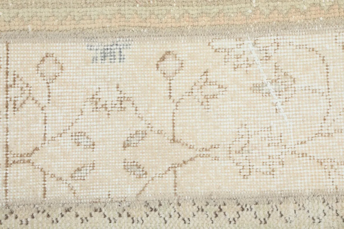 Close-up of the low wool pile and intricate weaving of a beige patterned section.