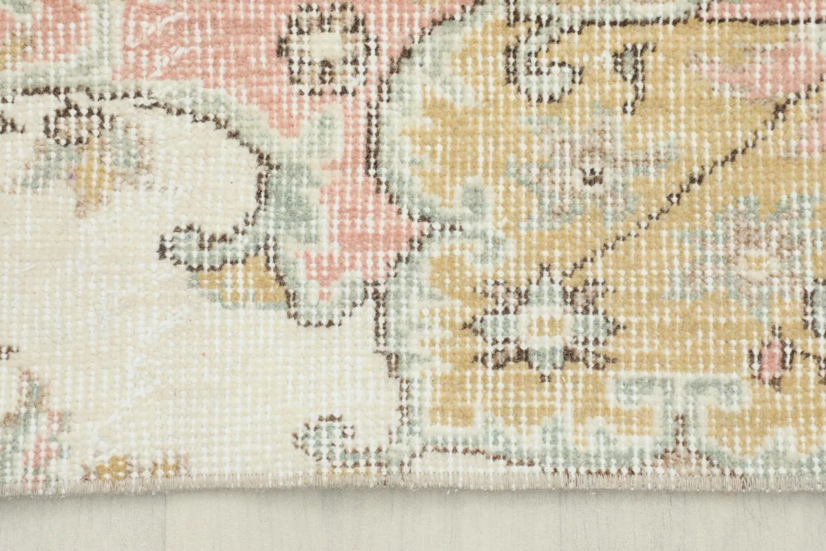 Close-up of the faded wool pile, showing intricate patterns in yellow, pink, and ivory