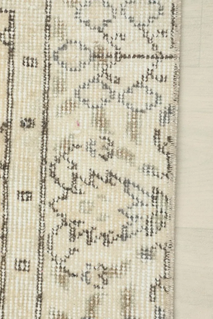 Close-up of a geometric pattern within a beige patch, illustrating the vintage wear and knotting