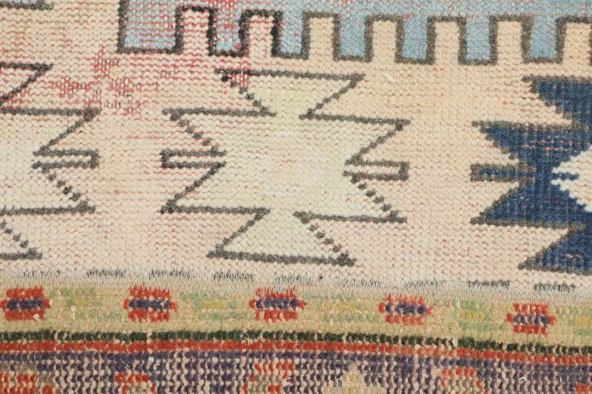 Macro shot of the wool pile, showing intricate geometric patterns in beige, blue, and green on a light background.