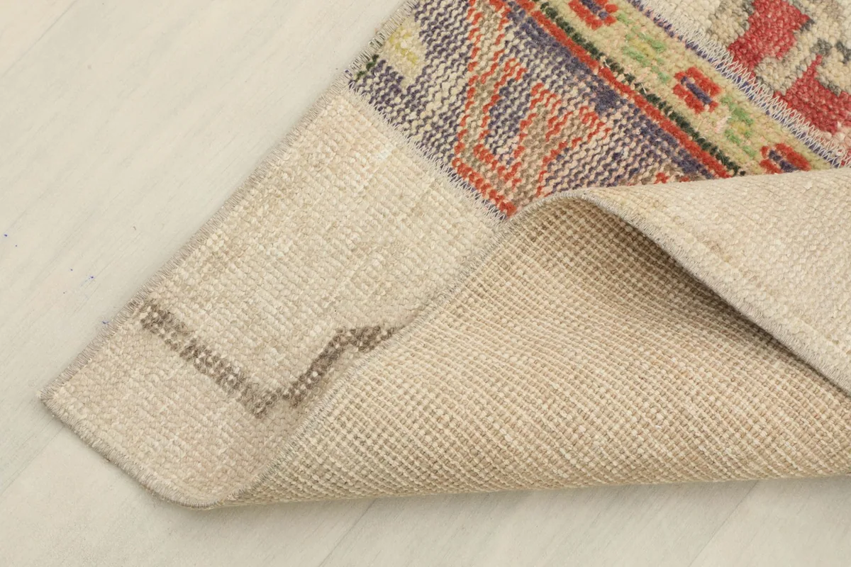 Corner of the rug folded back, revealing the sturdy cotton foundation and the texture of the wool pile.