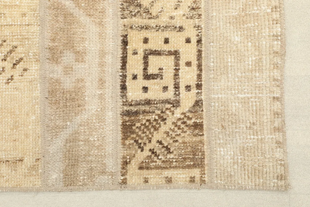 Close-up detail of the hand-knotted wool pile and geometric patterns in tan and brown.