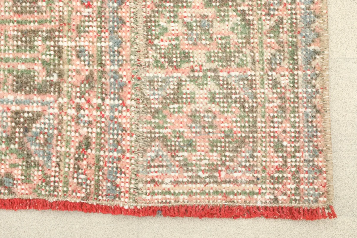 Close-up detail of the rug's surface, showing the faded rose, olive, and blue geometric motifs and low pile.