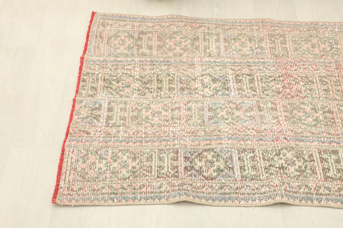 View along one side of the rug, showing the geometric patterns extending to the woven edge and red overcasting.