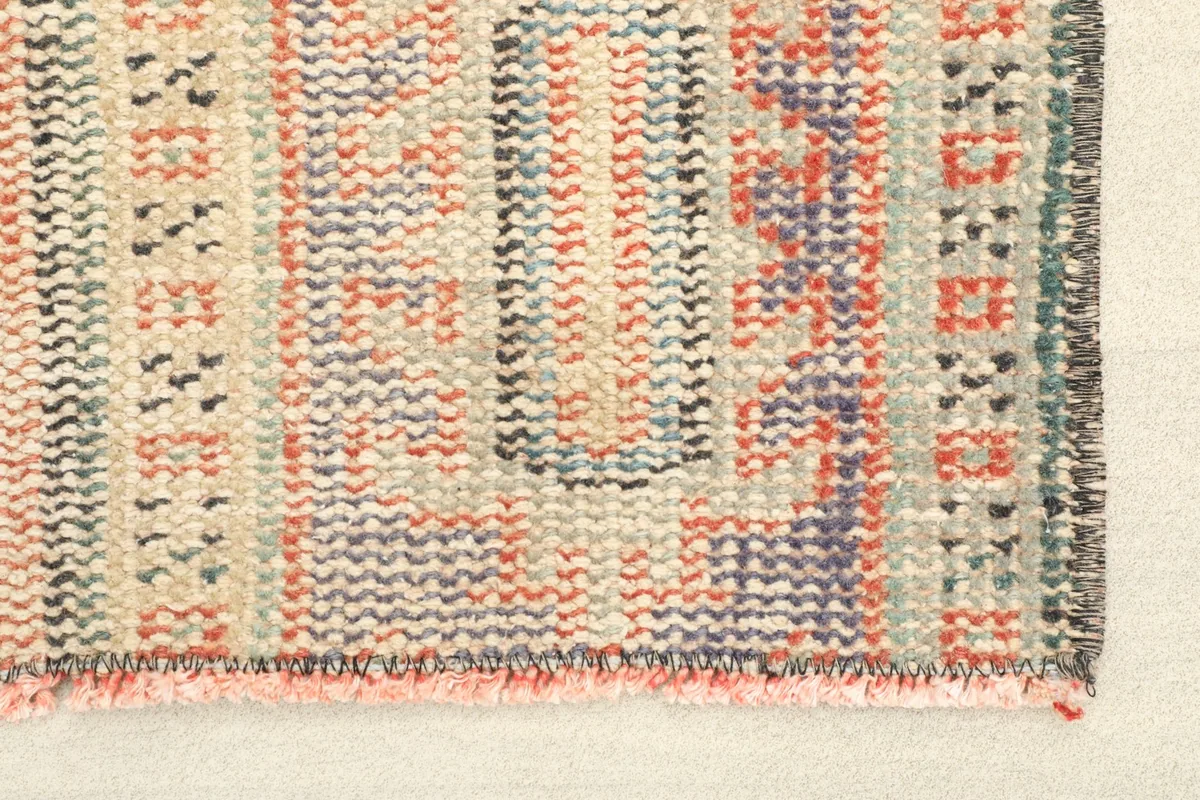 Close-up detail of the rug's texture and colors, showing the rose, purple, and beige wool knots.
