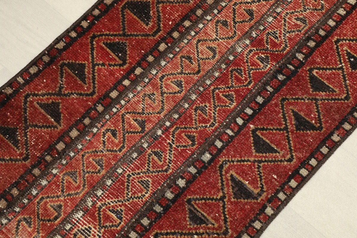 Close-up detail of the hand-knotted wool pile, showing red and black geometric motifs.