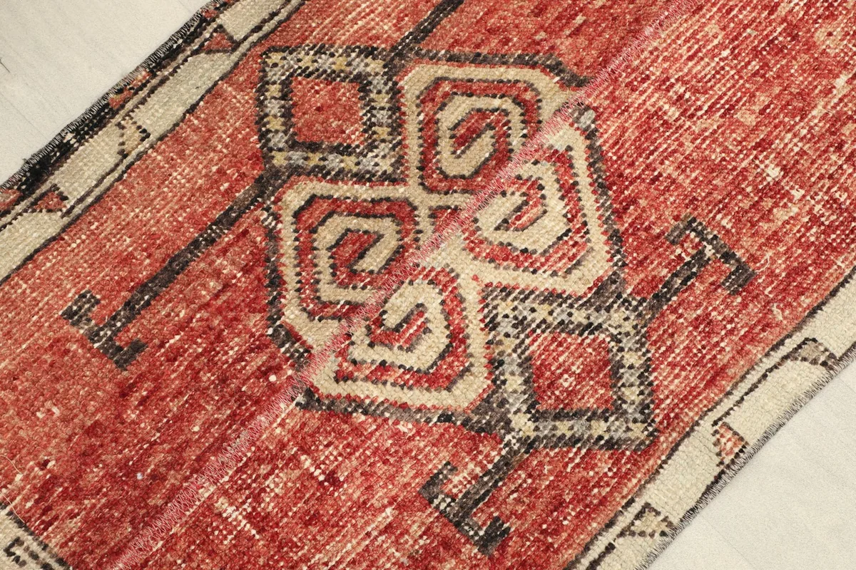 Angled view of the rug, highlighting the distressed red pile and beige geometric pattern.