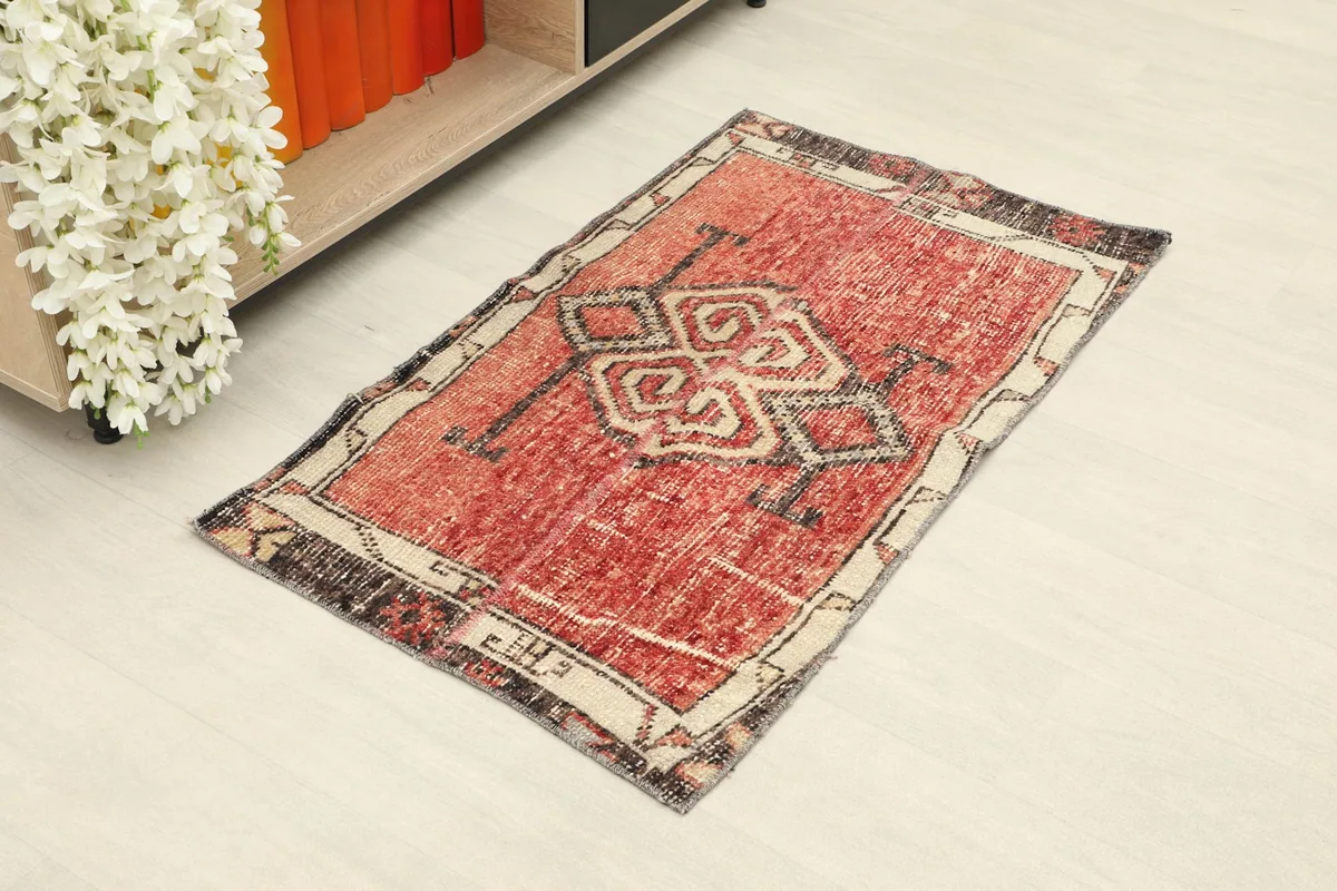 Vintage red Anatolian rug with geometric motifs placed on a light floor next to a shelf.