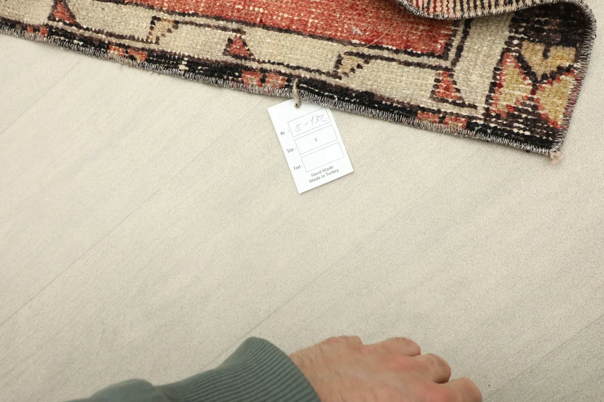 Hand pointing to the care tag attached to the vintage red rug, showing product information.