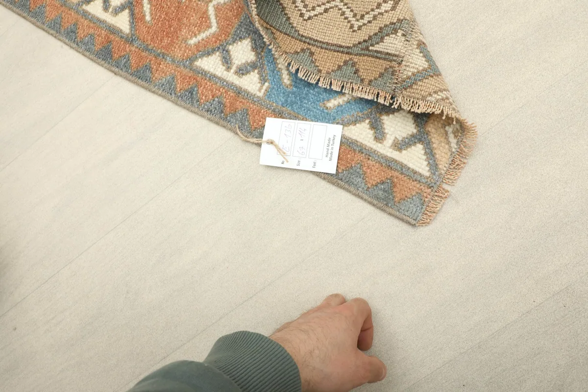 Hand next to the rug to show scale, highlighting the texture and low pile