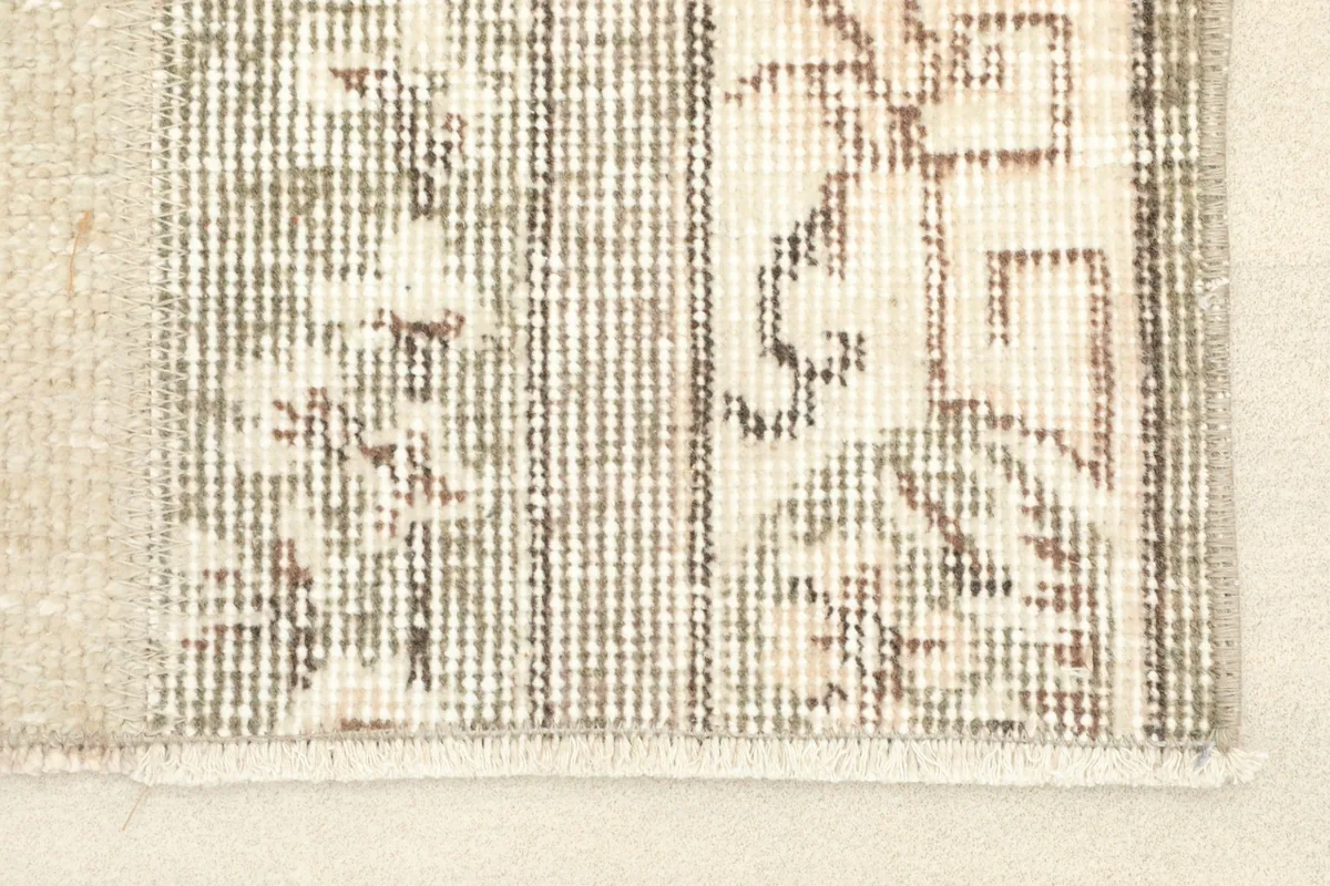 Close-up detail of the hand-knotted wool pile, showing beige, gray, and brown geometric motifs.