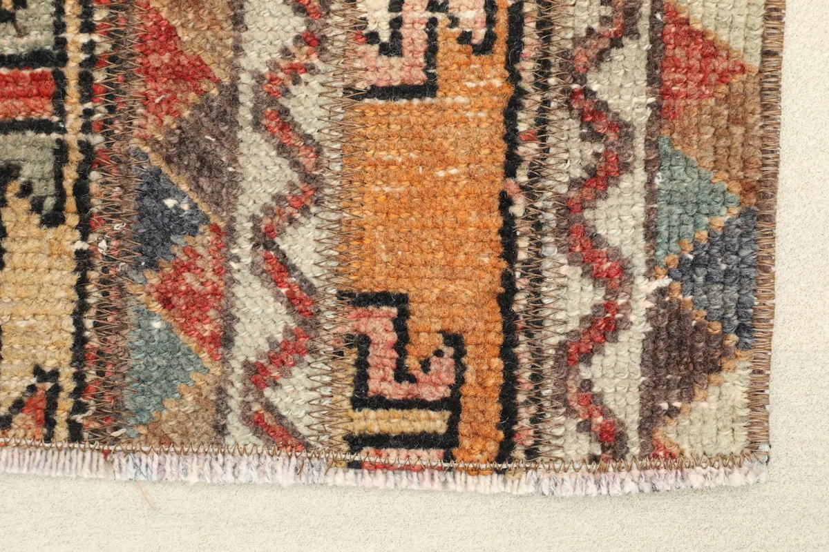 Close-up detail of the hand-knotted wool pile, showing orange and beige tones with tribal patterns.