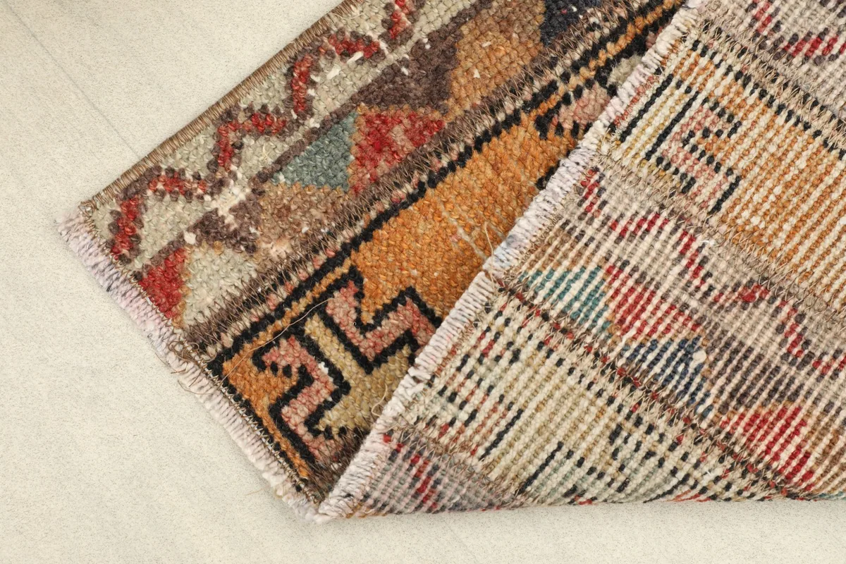 View of the rug's backside and a corner folded, revealing the hand-knotted cotton foundation and pile structure.