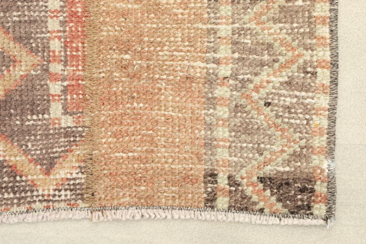 Close-up detail of the hand-knotted wool pile and cotton foundation, showing rose, brown, and gray tones.