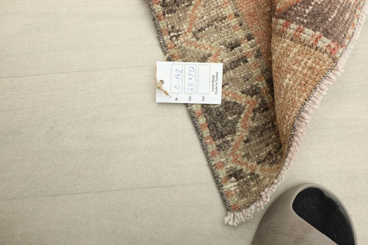 Corner of the rug with a tag, showing the product details and a neutral-colored shoe for scale.