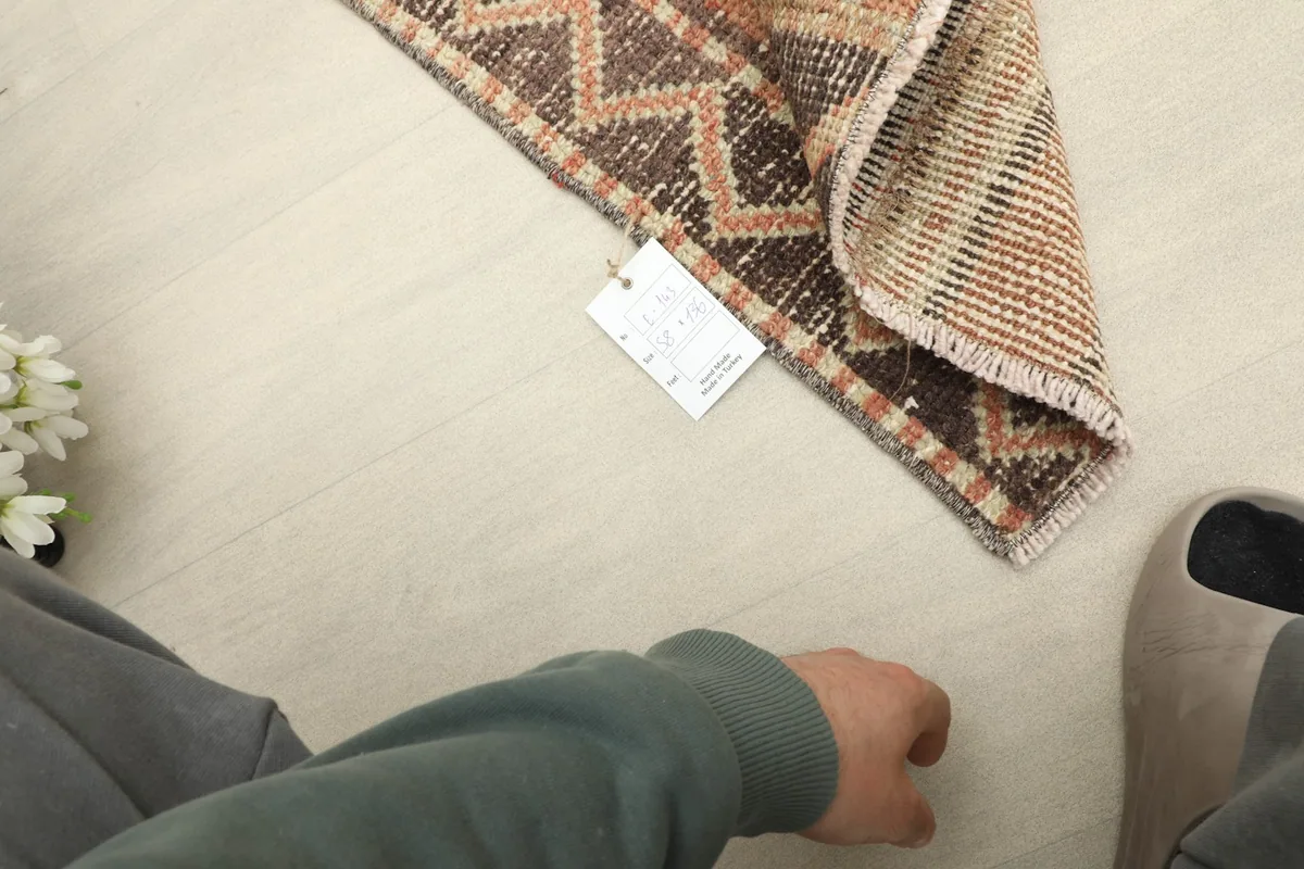 Overhead view of a folded corner with a tag, showing the rug's texture in context with a hand.