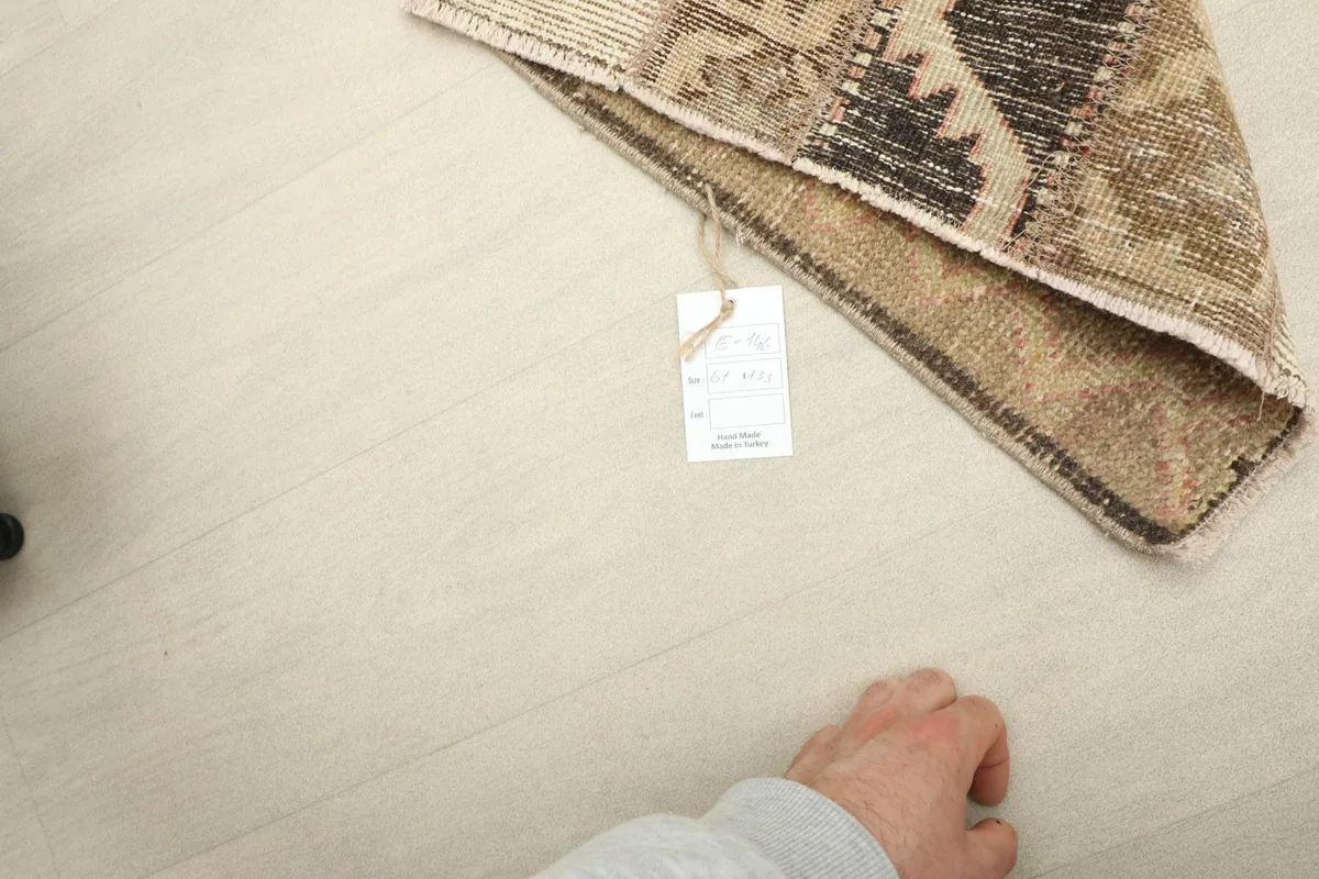 Hand next to the folded rug, indicating the mini size and showing the product tag