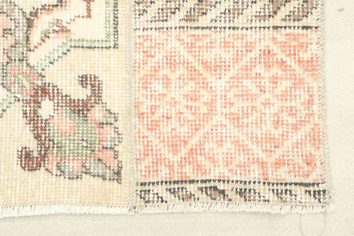 Close-up detail of the rug's patchwork section with orange geometric patterns and beige wool pile.