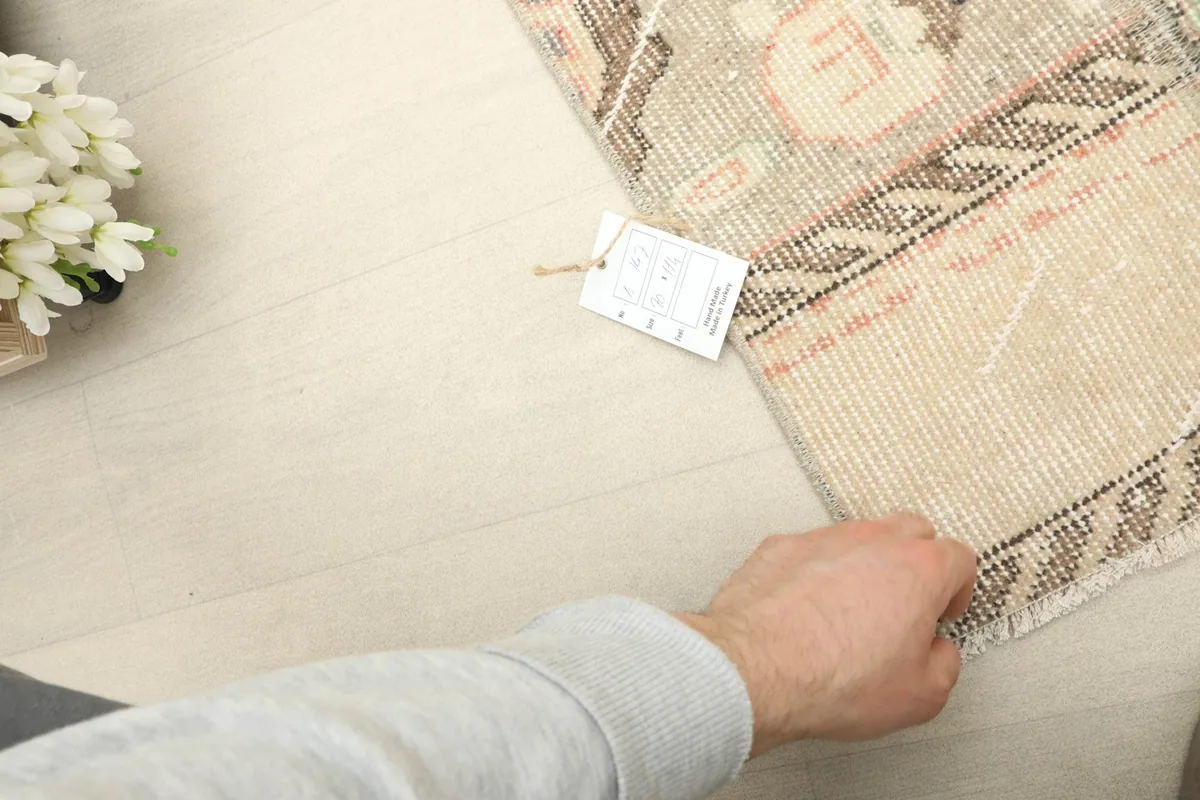 A hand gently touching the rug's edge, indicating its size and texture next to a product tag.