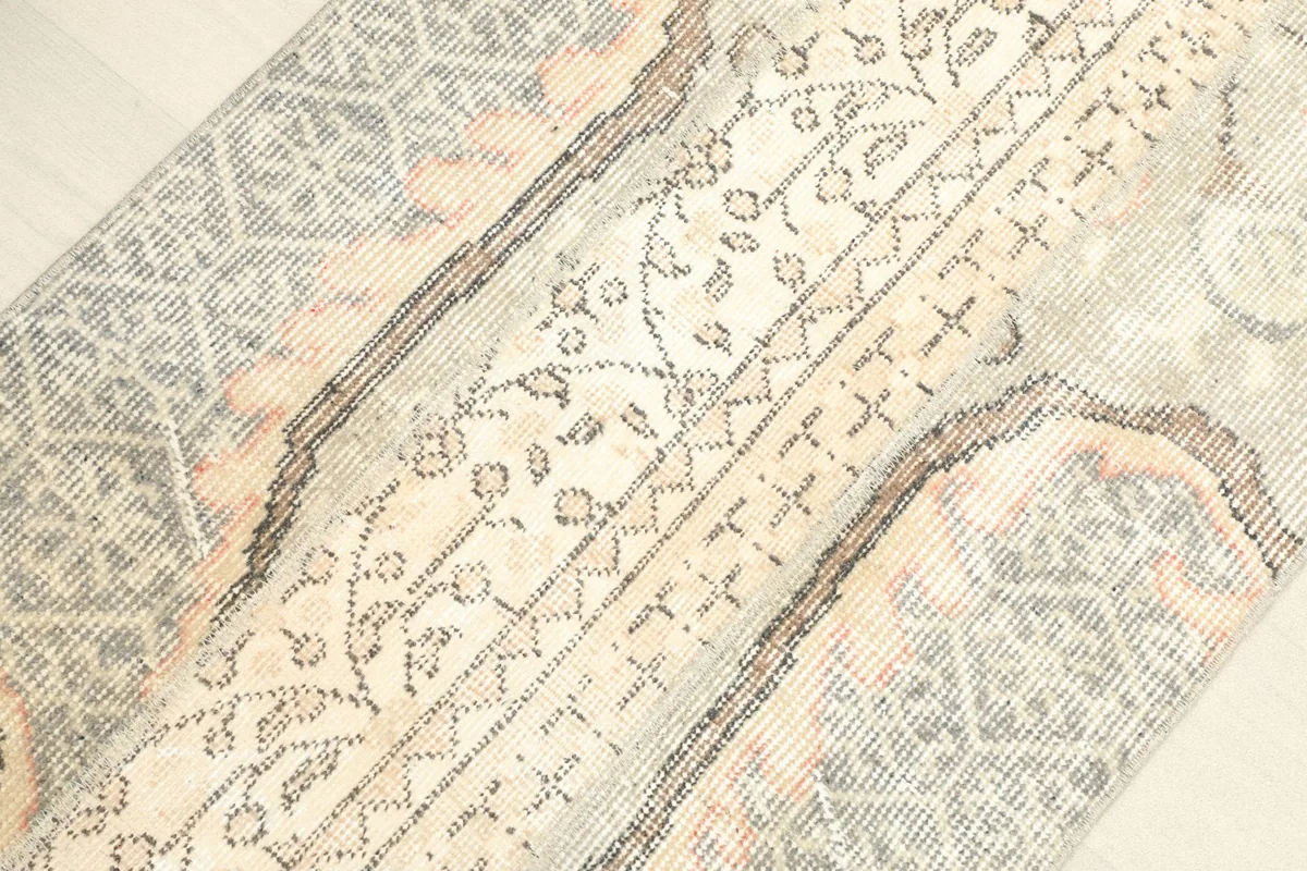Angled view highlighting the central ivory panel and the faded gray and rust sections of the rug.