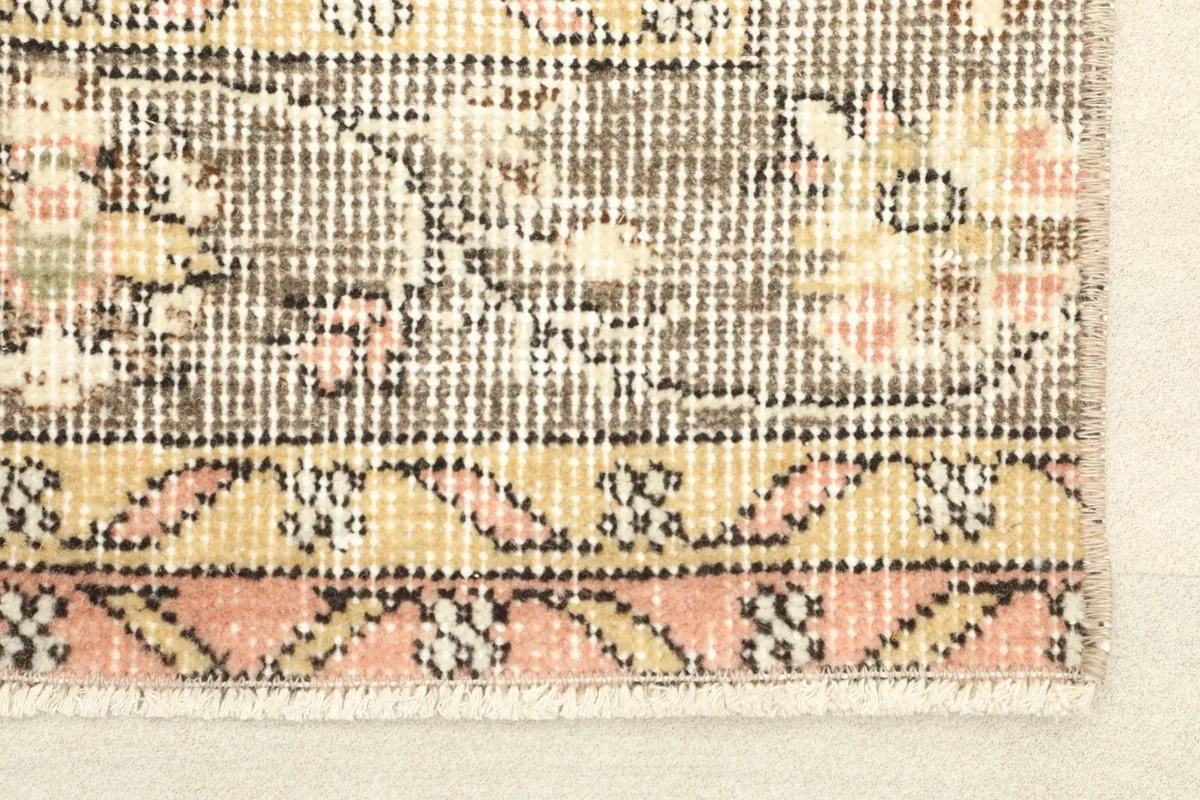 Close-up detail of the rug's border, showcasing the geometric patterns and colors like pink, gold, and gray.