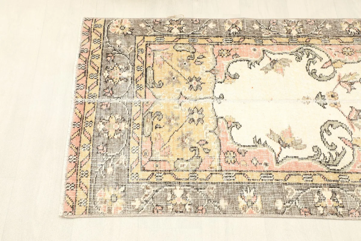 View of the rug's side border, featuring a blend of pink, gold, and gray geometric designs.