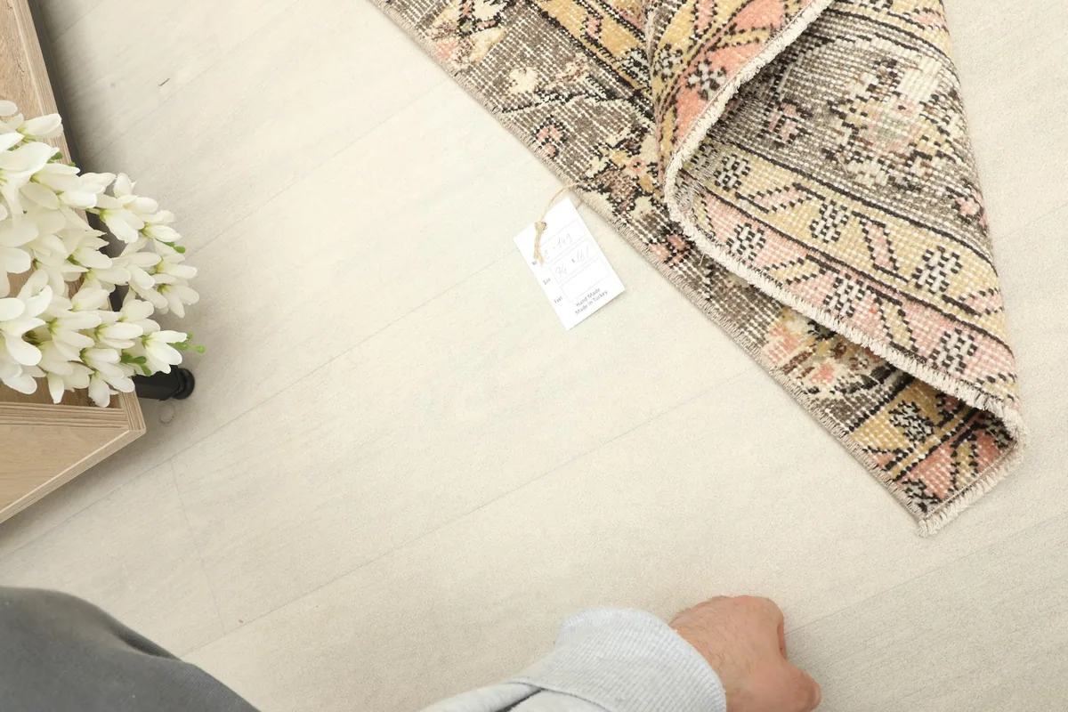 Corner of the rug with a hand visible, illustrating the scale and texture of the vintage wool pile.