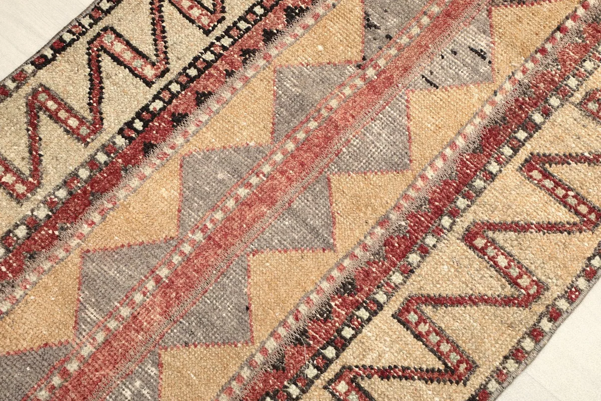 Angled view of the rug's geometric patterns and color variations, including red, gray, and tan.