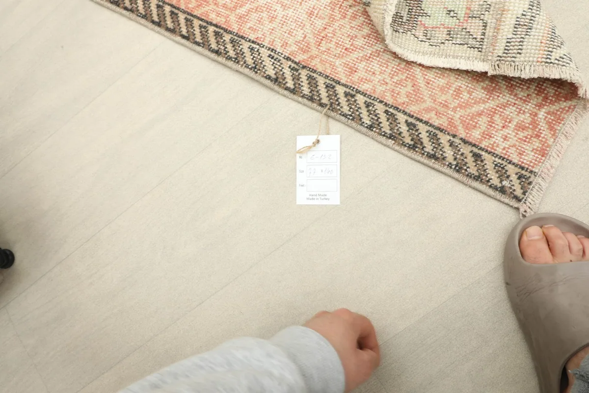 Overhead view of the rug's edge on the floor, with a hand and foot for scale.