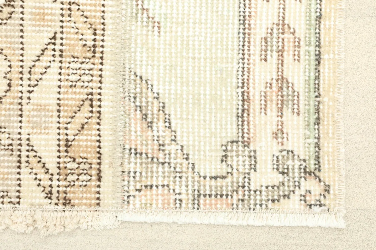Close-up detail of the rug's short fringe and intricate geometric and floral patterns in ivory, beige, and brown.