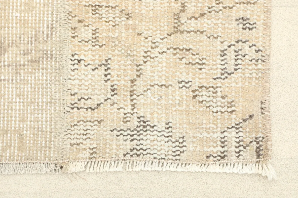 Close-up of the rug's fringe and the intricate hand-knotted texture with faded gray patterns.