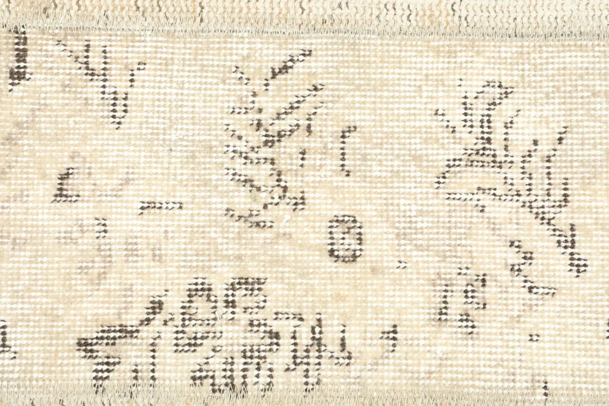 Detailed view of the wool pile and the subtle, faded gray and brown patterns on the beige field.