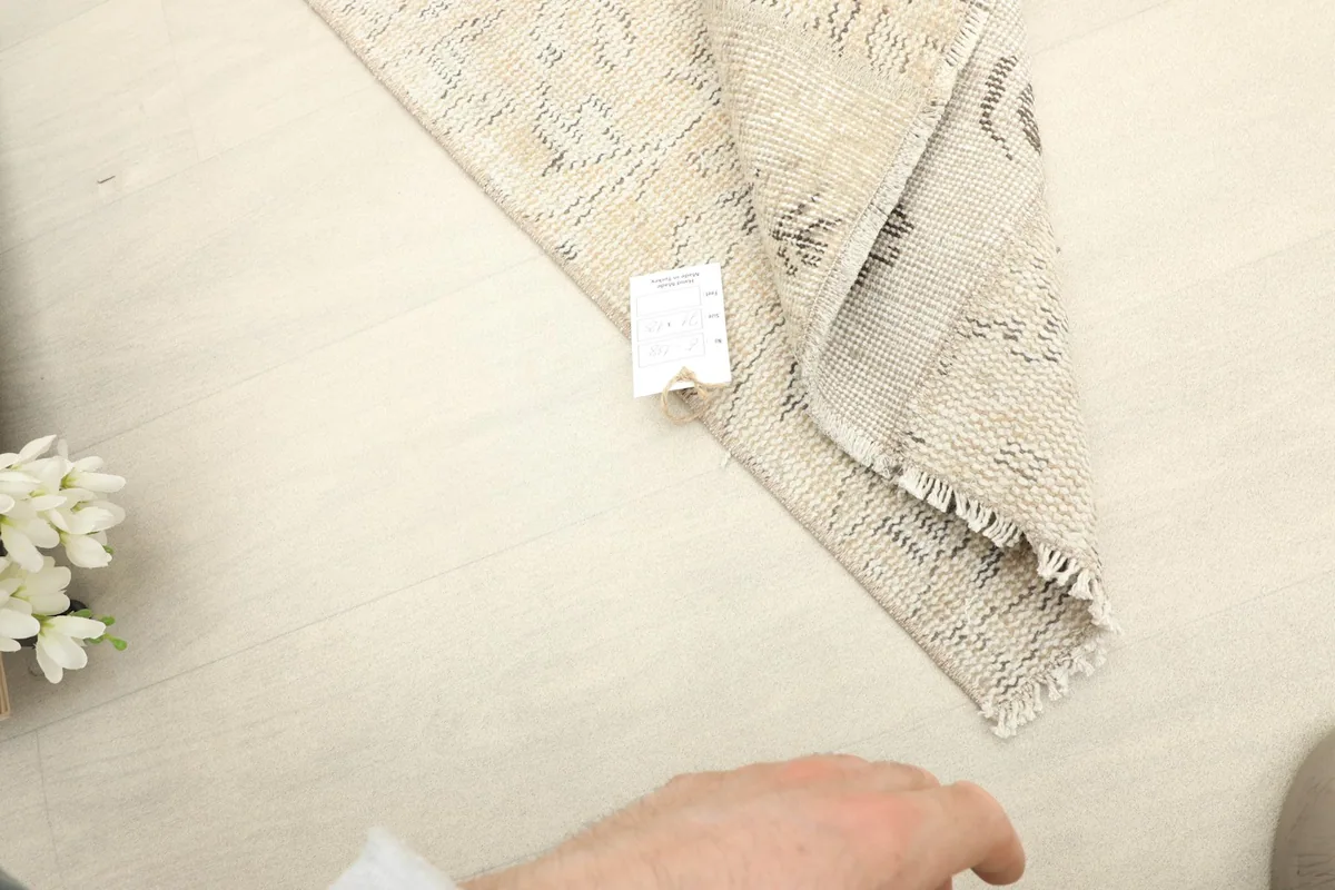 A hand holding a tag near the folded rug, indicating its quality and origin.