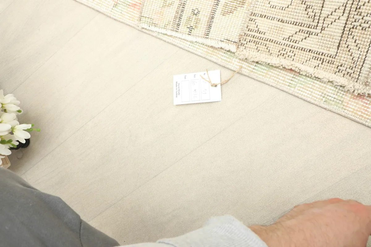 A small tag resting next to the folded rug on a light wooden floor, indicating its authenticity.