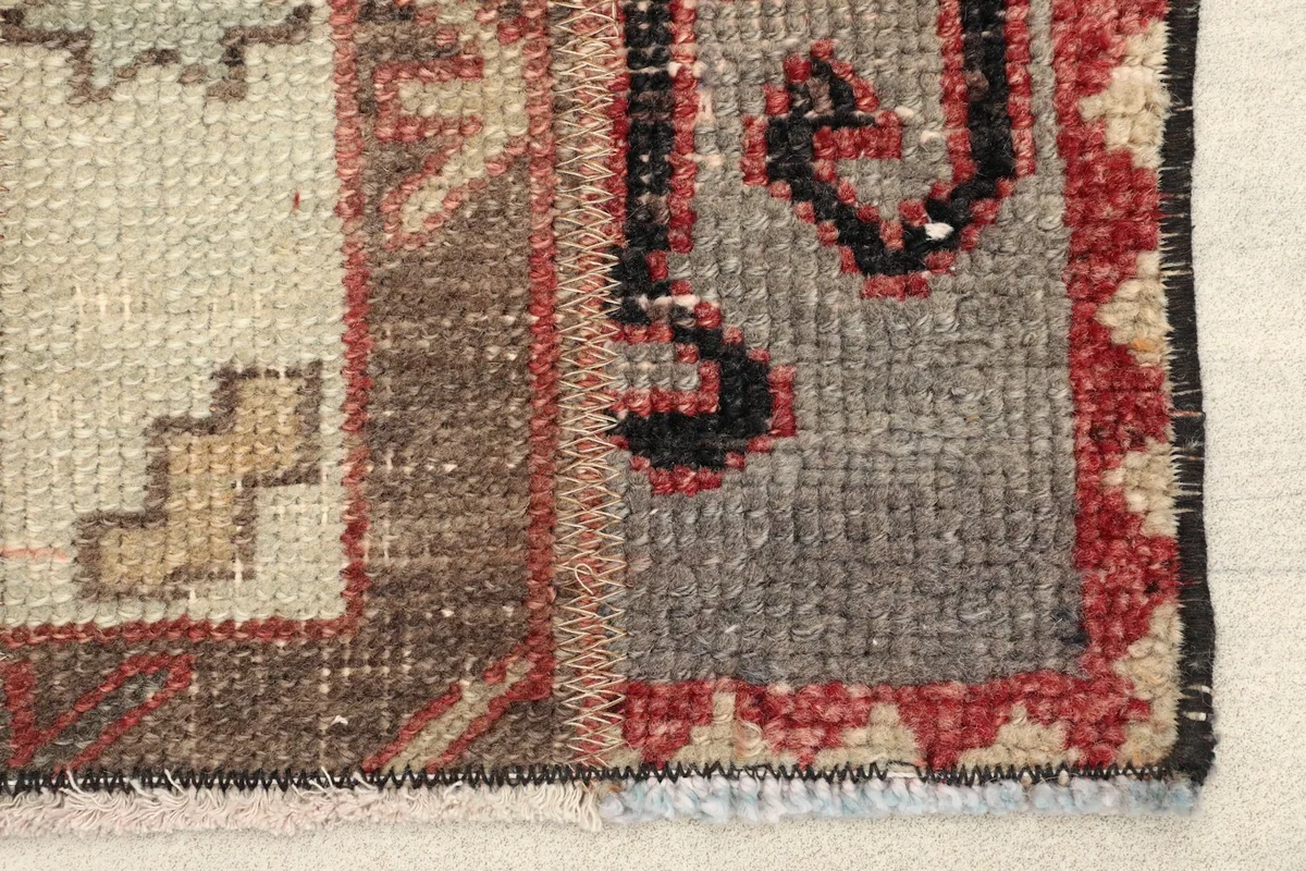Close-up detail of the rug's edge, showing the red, black, and gray wool pile and cotton foundation