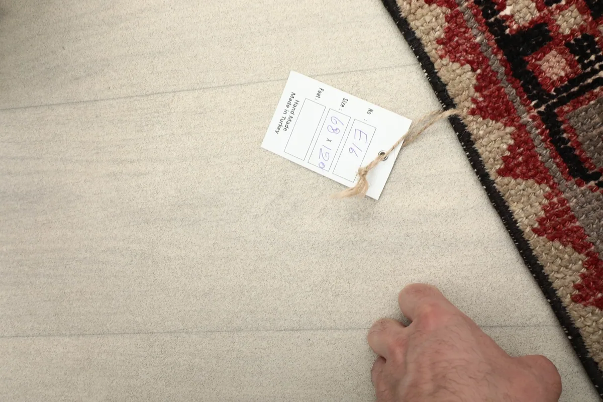 Hand pointing to the product tag with rug dimensions and origin information