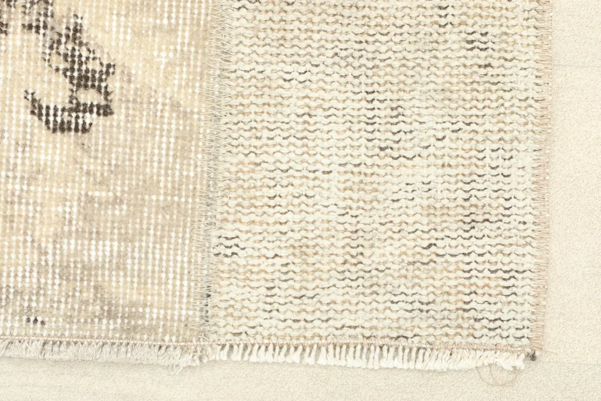 Close-up of the short, worn fringe and the subtle texture of the beige wool pile.