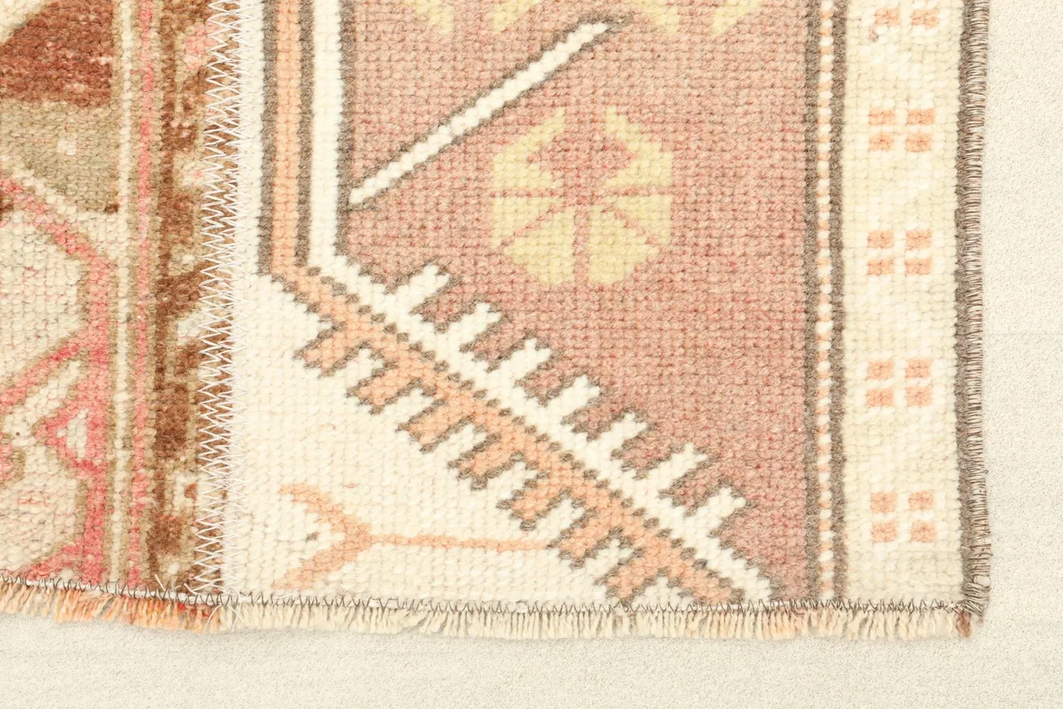 Close-up detail of the rug's corner, showing rose, beige, and ivory geometric motifs and fringe.