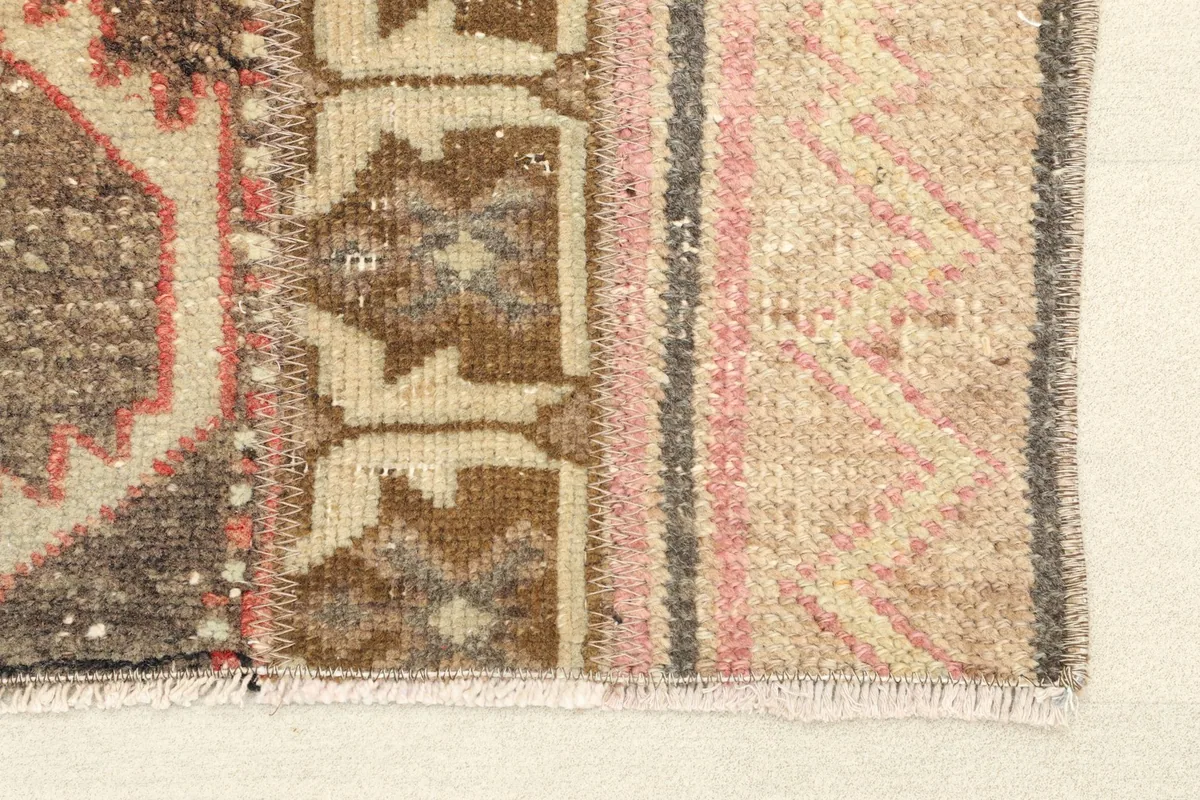 Close-up detail of the rug's edge, showing the fringed finish and the varied rose, brown, and beige tones.