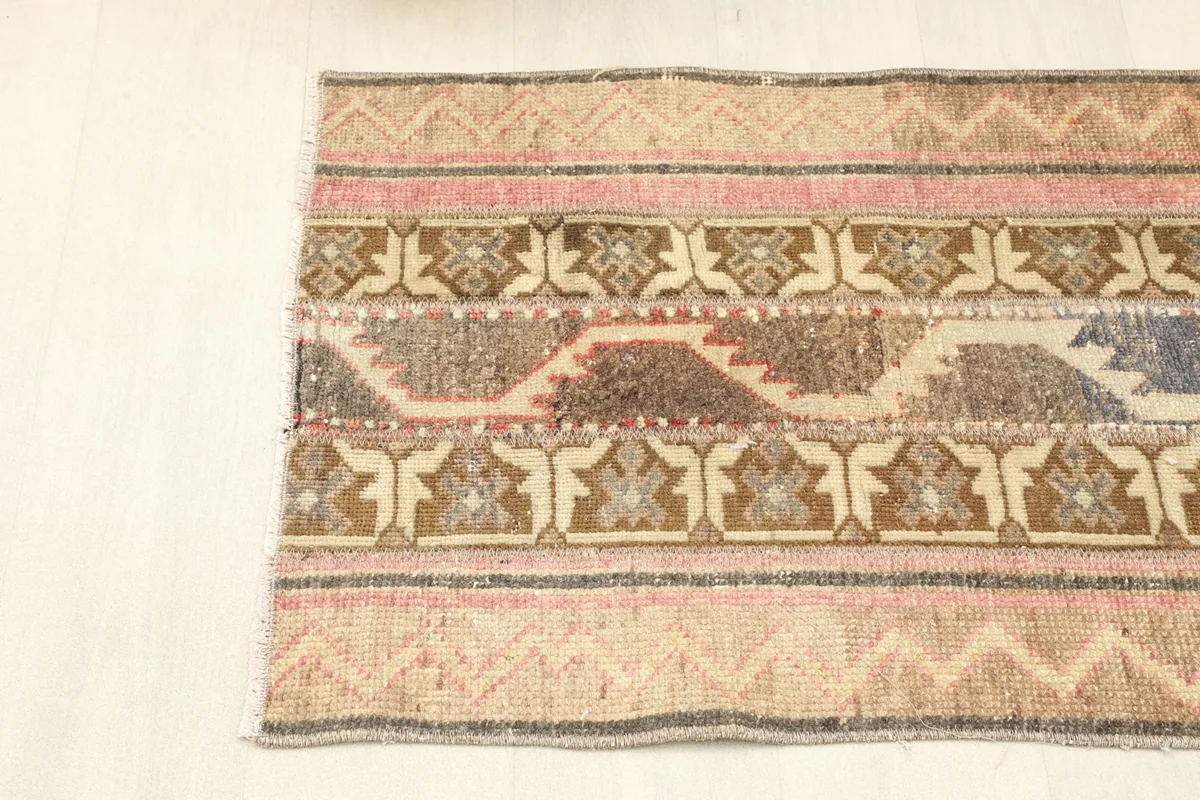 Detail of one end of the rug, focusing on the striped borders and geometric motifs in rose and brown.
